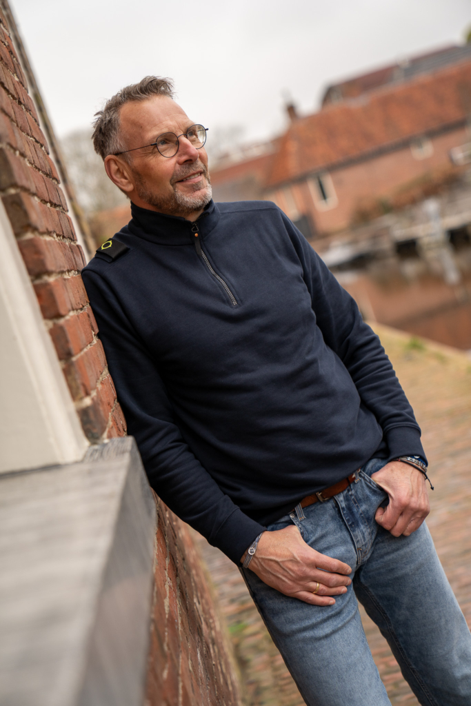 volwassen man casual leunend tegen muur in donkerblauwe half zip sweater van exclusief herenmerk Ma-Strum in het mooiste dorp van Nederland, Winsum Gr.