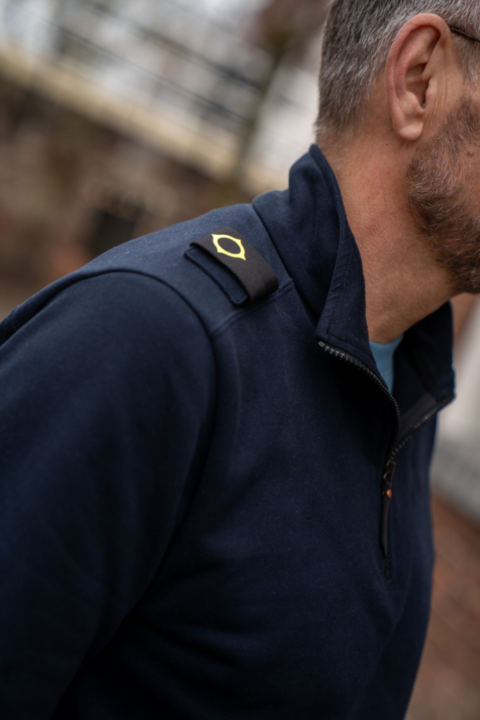 volwassen man met bekend logo van populair herenkleding merk Ma-Strum. Logo is bekend van Stone Island. Donkerblauwe sweater met halve rits. Duurzaam winkelen in Winsum. Groningen