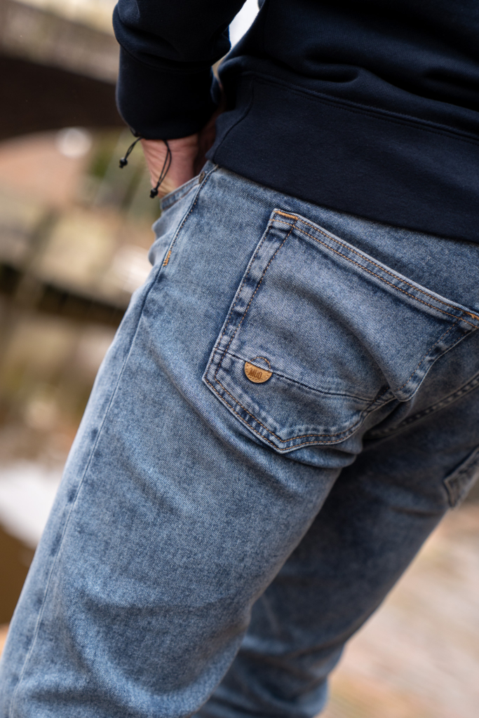 achterkant broekzak van MUD jeans spijkerbroek, details van organic cotton, achtergrond water in Winsum, Groningen, duurzame kleding, gerecyled jeans voor heren en dames