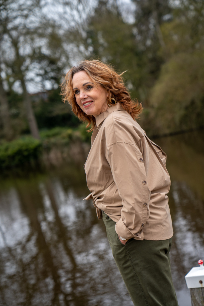 dame kijkend over water gekleed in lichtbruine camel blouse met knopen op achterkant mouw