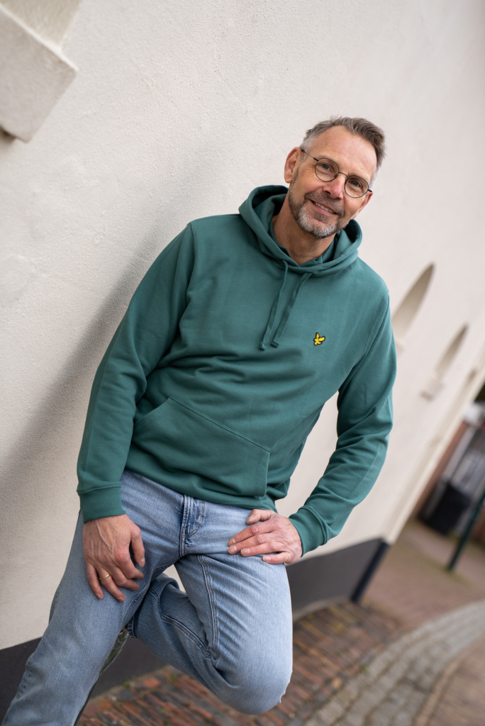 man leunend tegen witte muur in Winsum, draagt een hooded sweater Lyle & Scott in groen, jeans is van G-STAR recht model 'Mosa'