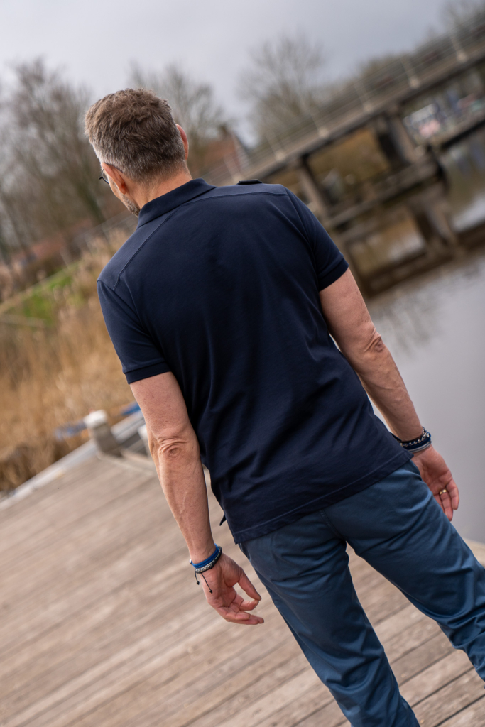 achterkant van volwassen man bij het water in Winsum, duurzame kleding van MUD jeans en exclusieve polo van Ma-Strum in donkerblauw