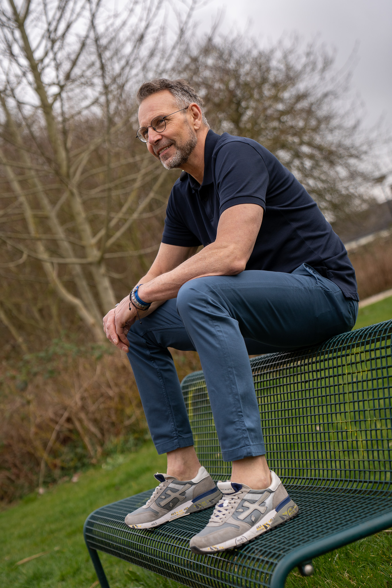 volwassen man zitten op bovenkant bankje in de natuur in Winsum, draagt een donkergroene petrolkleur MUD jeans chino model met gerecyclede katoen gemaakt