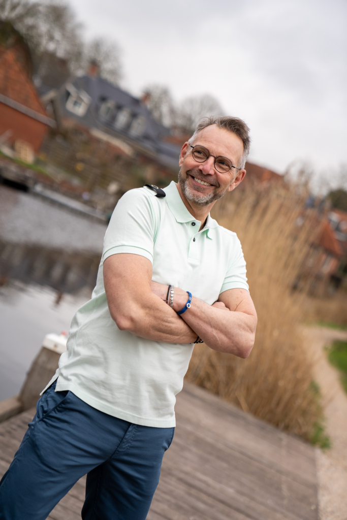 herenmode, man showt lachend met armen over elkaar mintgroene polo met korte mouw Ma-Strum op een petrolkleur broek van MUD jeans