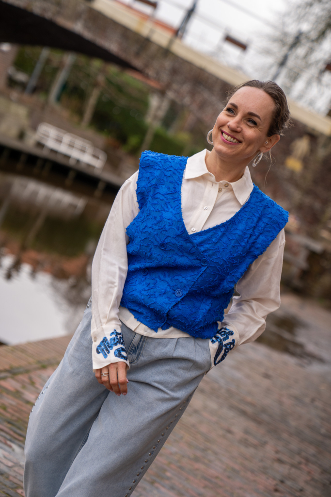 Sytha draagt POM blauw gilet met linnen witte blouse met pailletten tekst op boord