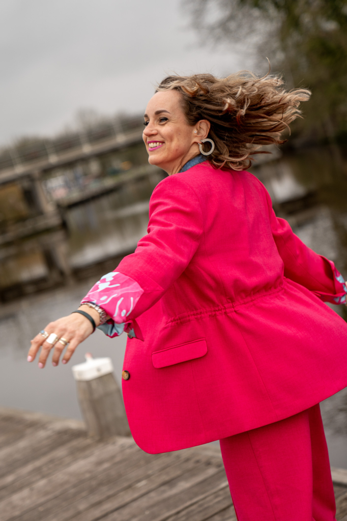 Vrouw kijkt blij en zwiert vrolijk met haar rose POM Amsterdam blazer