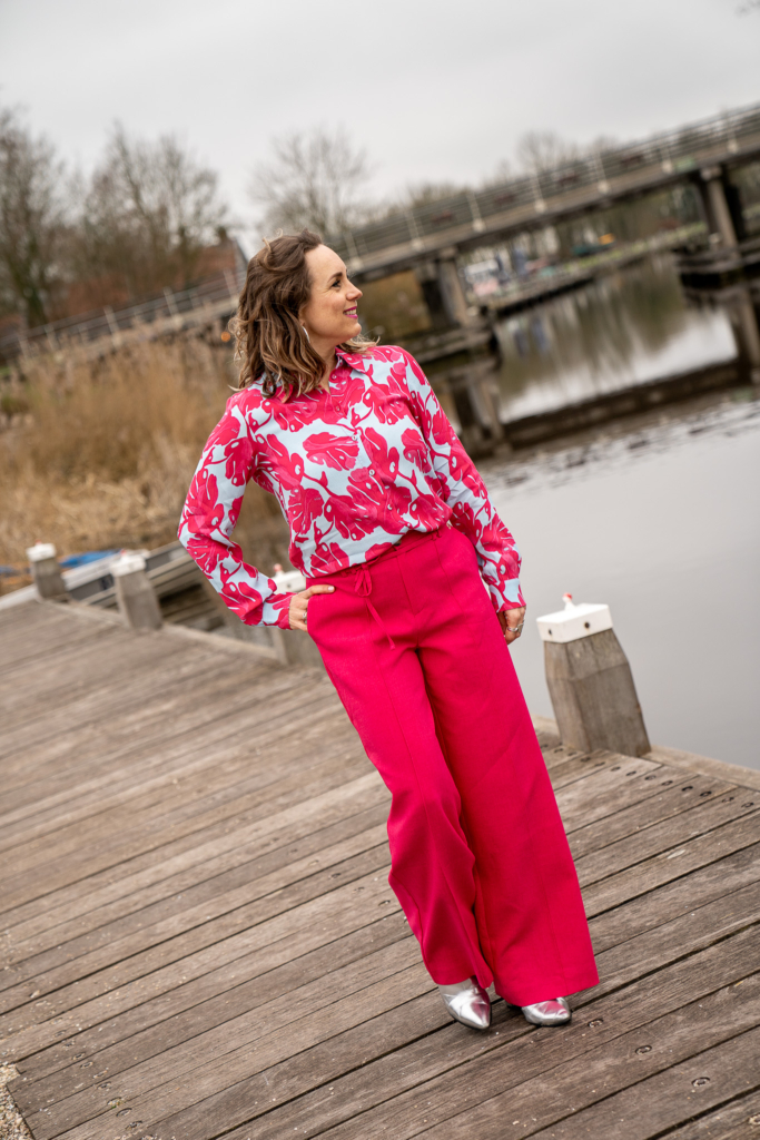 dame loopt langs water in blauw/rose print blouse grafische bloemen